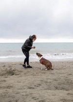امرأة ترتدي قناع وجه واقٍ تلعب مع كلب على شاطئ مهجور، في اليوم الرابع من إغلاق غير مسبوق في جميع أنحاء إيطاليا لإبطاء تفشي فيروس كورونا.  رويترز
