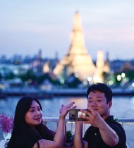 زوجان يلتقطان صورة سيلفي وخلفهما معبد وات آرون في مطعم على السطح على طول النهر في بانكوك.  ا ف ب